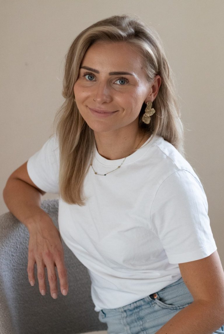 Virtual assistant Indy Jonge vrouw met blond haar, in een wit shirt, glimlachend en zittend op een stoel.